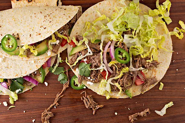 An overhead close up horizontal photograph of the making of some shredded beef tacos.