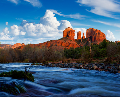 Cathedral Rock near Sedona during sunset. A nice red rock formation in the background, a blurred flowing creek in the foreground and bushes and trees alongside.