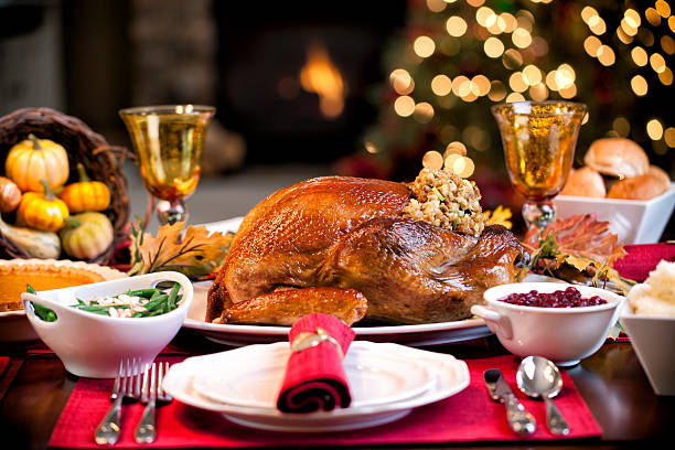 Close up of a turkey at a traditional Christmas dinner.  The natural light pours in from the inviting window framed by a decorated Christmas tree in the background.  Lit with candles, the feast is ready for its guests to indulge in a quintessential Christmas meal filled with turkey and pie.