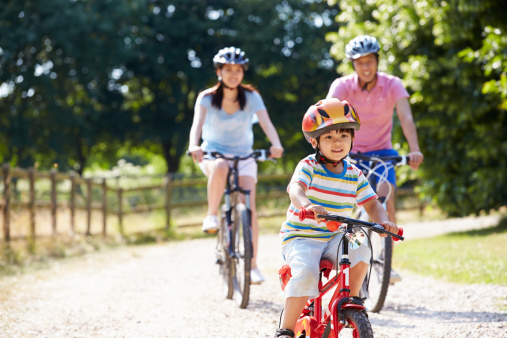 Asian Family On Cycle Ride In Countryside Wearing Helmet Having Fun