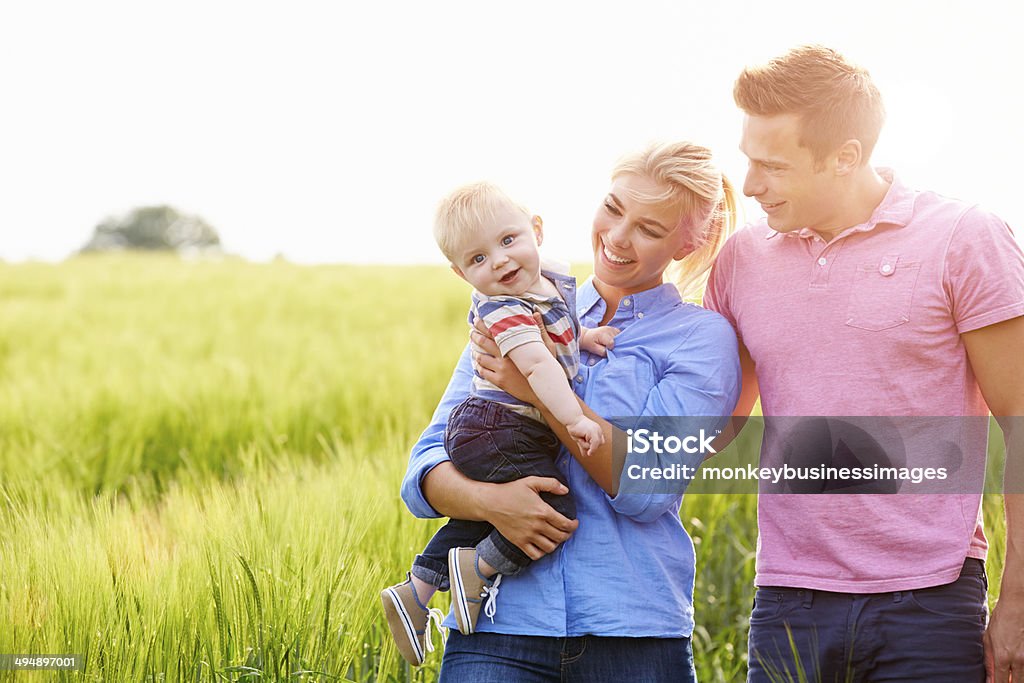 Family Walking In Field Carrying Young Baby Son Family Walking In Field Carrying Young Baby Son Smiling Family Stock Photo