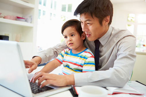 Busy Father Working From Home With Son Sat On Lap