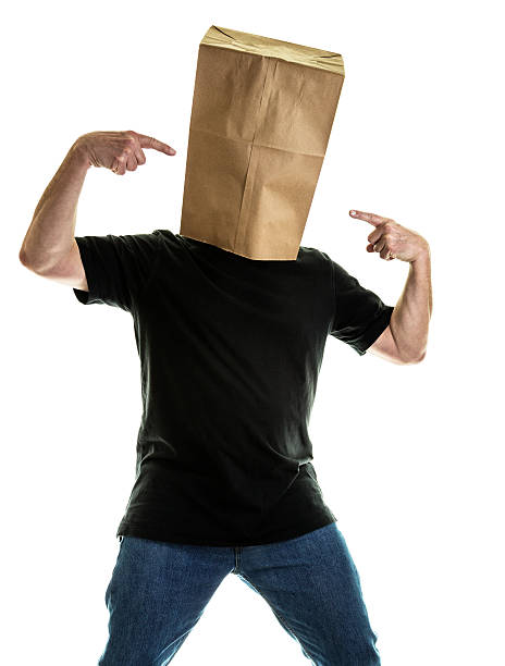 Anonymous Man Wearing Paper Bag Pointing At Head An anonymous - maybe embarrassed or frustrated sports fan? - man wearing a paper bag to cover his face and head is pointing his index fingers at the bag from both sides. He is wearing blue jeans and a casual black t-shirt. embarrassment unrecognizable person wearing a paper bag human head stock pictures, royalty-free photos & images