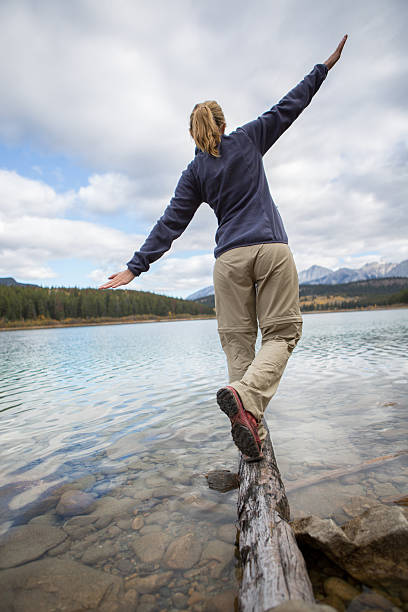 istock Young woman balances on log above lake 494903004