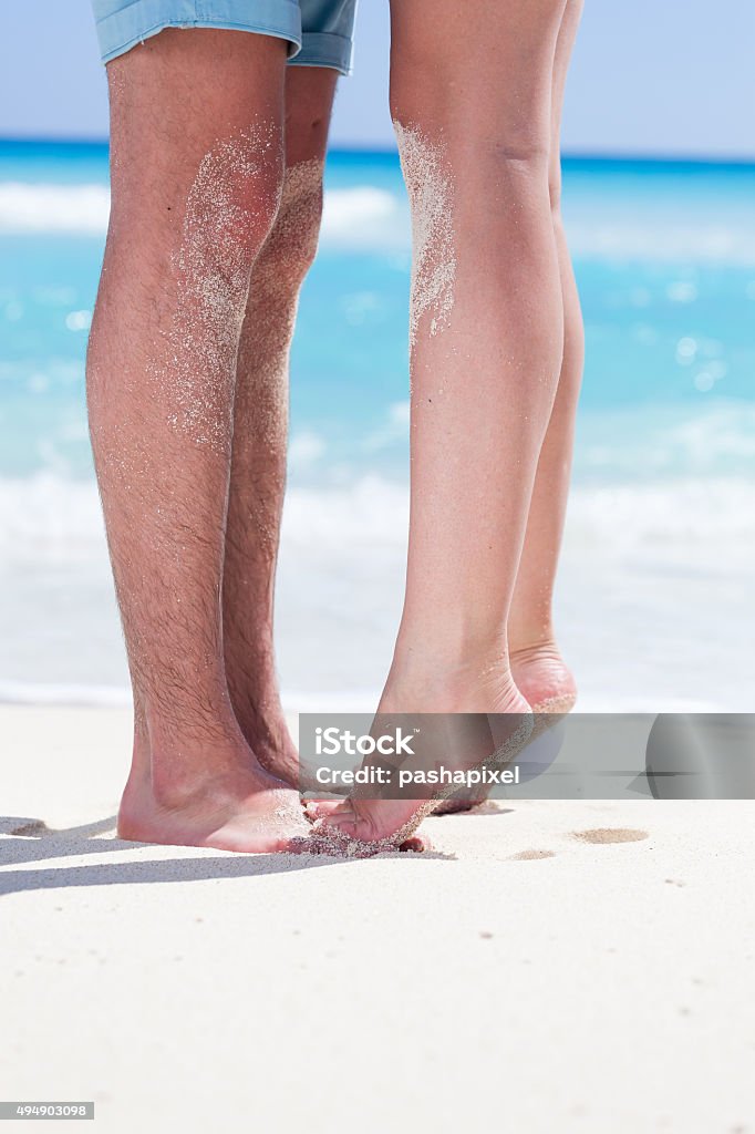 Couple of male and female legs on beach Woman's barefoot legs standing up tiptoe closeup to male foot and kissing on sandy beach with turquoise sea background, no face. Happy romantic holidays concept. 2015 Stock Photo
