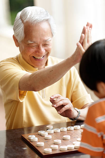 abuelo y nieto jugando xiangqi (ajedrez chino) - chinese chess fotografías e imágenes de stock