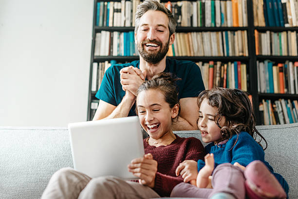 istock laughing little family on sofa looking tv at tablet computer 494940510