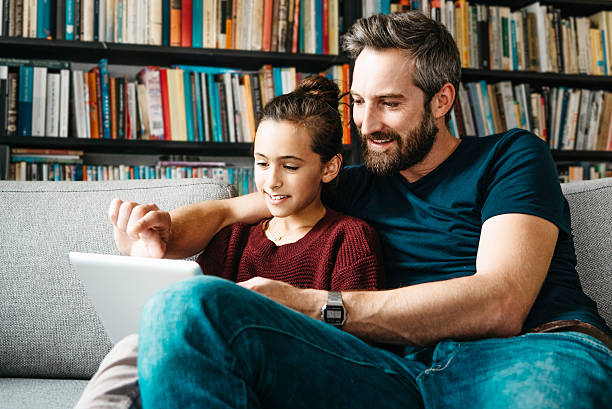 istock bearded dad with daughter tapping at digital tablet on couch 494940924