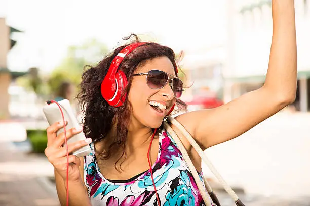 Photo of Mixed-race teen girl listens to music. Headphones, smart phone downtown.