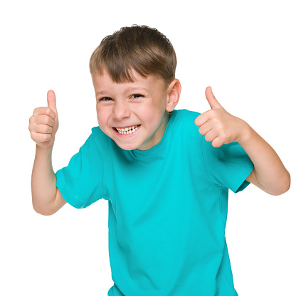 A laughing little boy holds his thumbs up against the white background