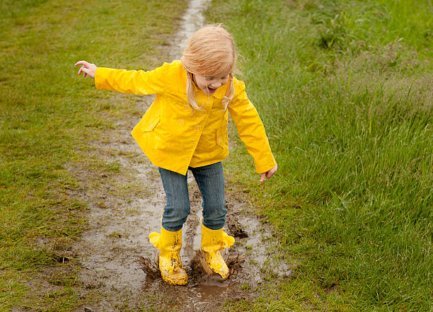 mädchen springt in eine pfütze schlamm - drenched raincoat rain clothing stock-fotos und bilder