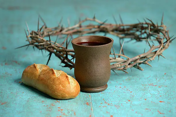 Bread, cup of wine and crown of thorns on old table