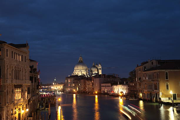 Venice, Italy - November 20, 2024: Waterfront scene features illuminated buildings and boats reflecting on the water, creating a tranquil ambiance at night