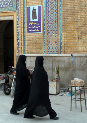 Qom, Iran - October 18, 2011. Women in Iran have to wear Tschador. A poster at the entrance of the Holy City reminds them. The picture shows two women underneath the poster