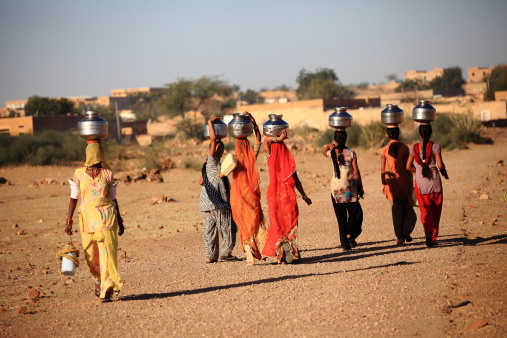 Rajasthan, India -February 27, 2013 : women lugging a water pot on their head . Due to the lack of piped water, poor tribals have to fetch water from its natural sources.