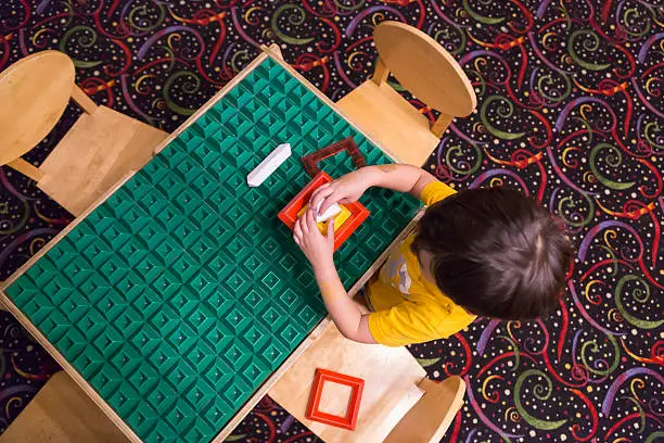 Overhead of Mixed-race Boy Sitting at a Work Table Playing with Building Blocks Toys.