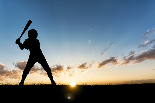 A young baseball player ready to swing as the game carries into the night. Hand drawn silhouette.