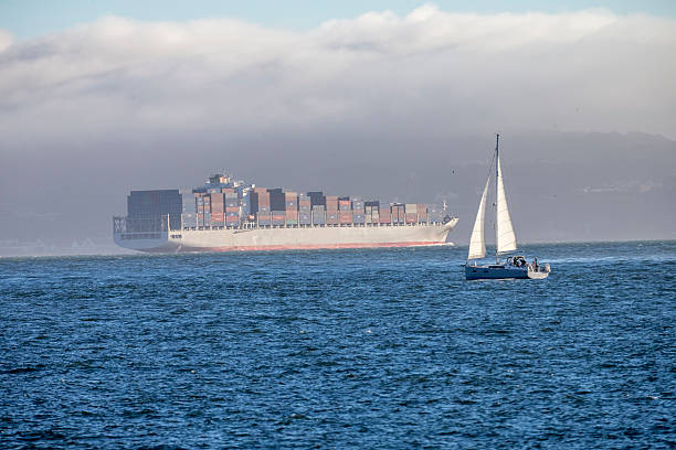 View over dark ruffle sea against clear blue sky and small white sail far away.