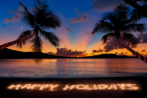 Happy Holidays made with Christmas lights at a Caribbean beach during dramatic sunset