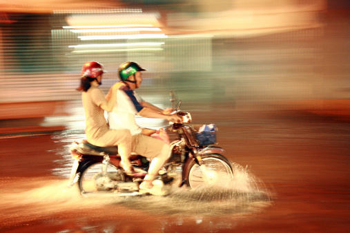 Ho Chi Minh City, Vietnam - October 15, 2009: This photo shows a Vietnamese couple riding their motorbike on a flooded street at night during the monsoon season. Blurred motion through panning technique.