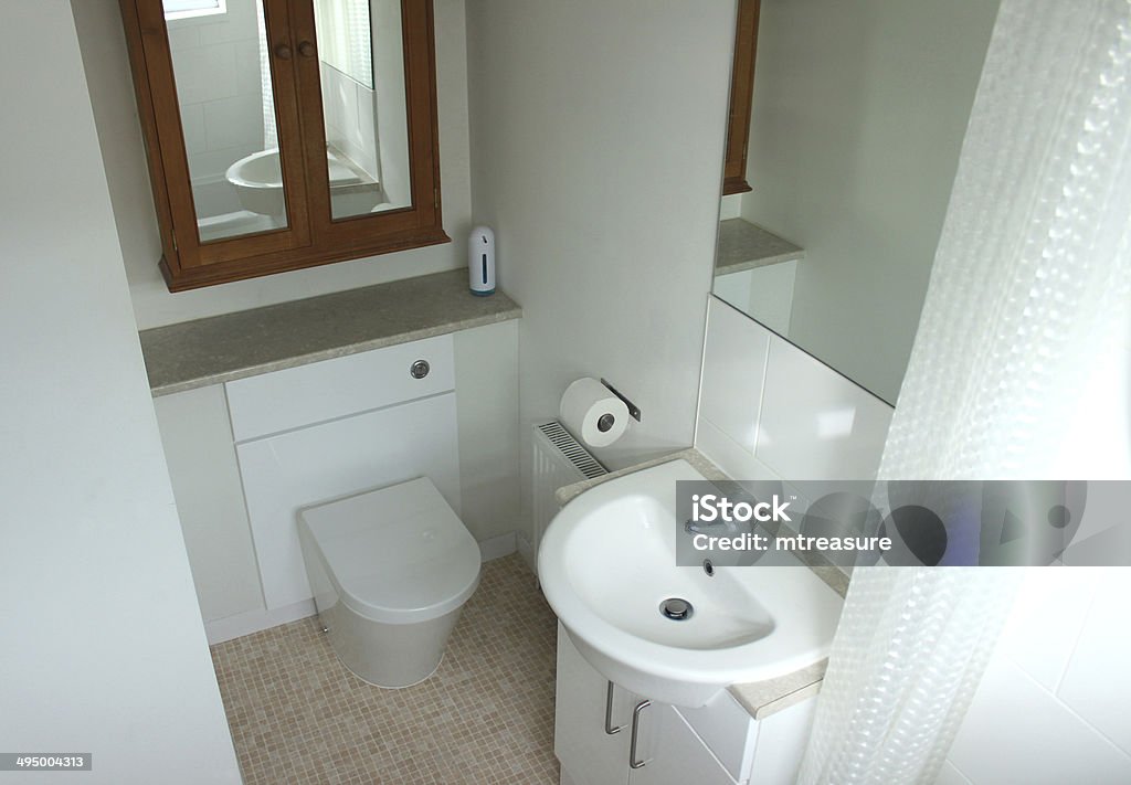 Image of a modern en suite bathroom with white sink Photo showing a modern en suite bathroom, with white ceramic sink and toilet, large pine cabinet, mirrors, homemade art work, mosaic vinyl floor and trendy soap dispenser. Luxury Stock Photo