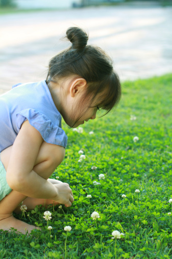 girl sitting on lawn picking clover flowers