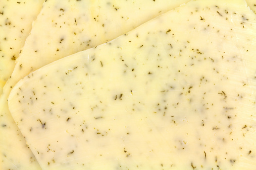 Close view of several slices of havarti cheese with dill seasoning.