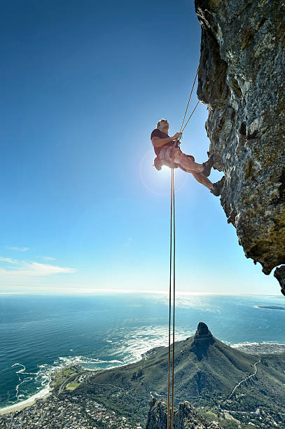 escalador abseiling over precipice mira en pared de roca - rápel fotografías e imágenes de stock