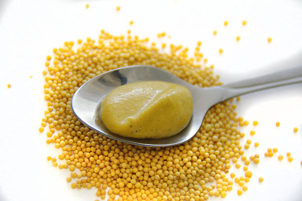 Small teaspoon with mustard on mustard seeds Small teaspoon with mustard on yellow mustard seeds dijonnaise stock pictures, royalty-free photos & images