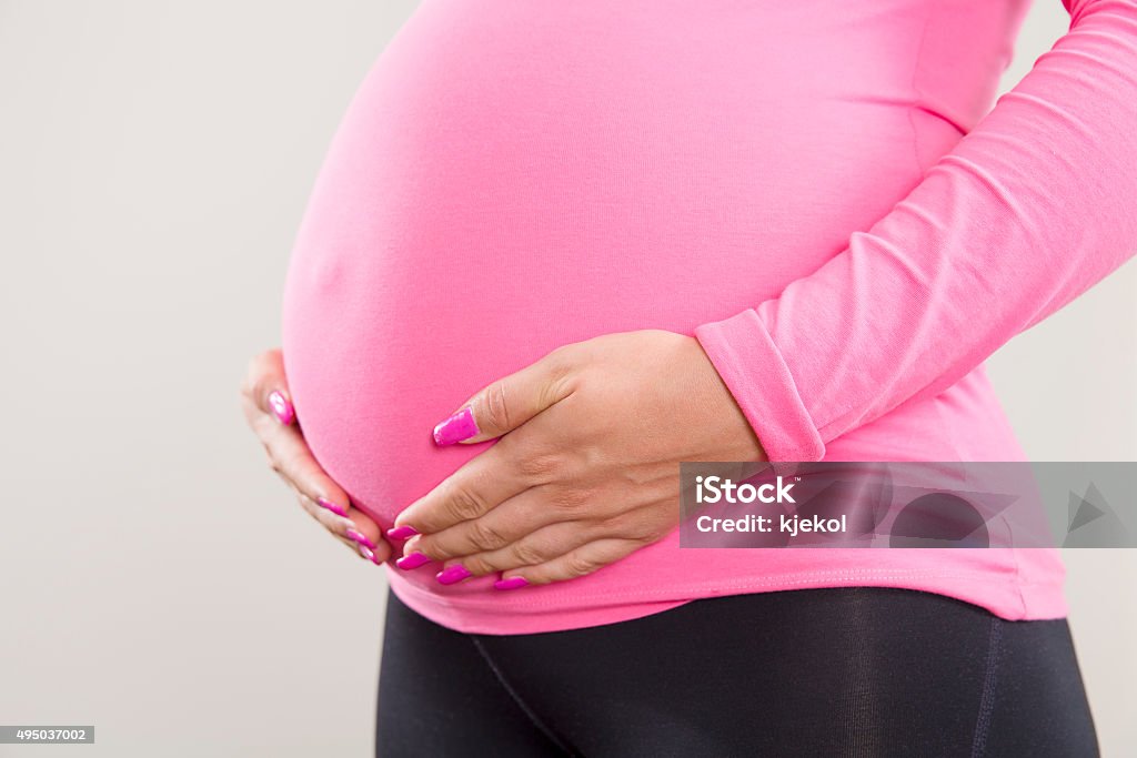 Pregnant woman holds on her swollen belly Close-up of an pregnant woman holding hands on her the swollen tummy. 2015 Stock Photo