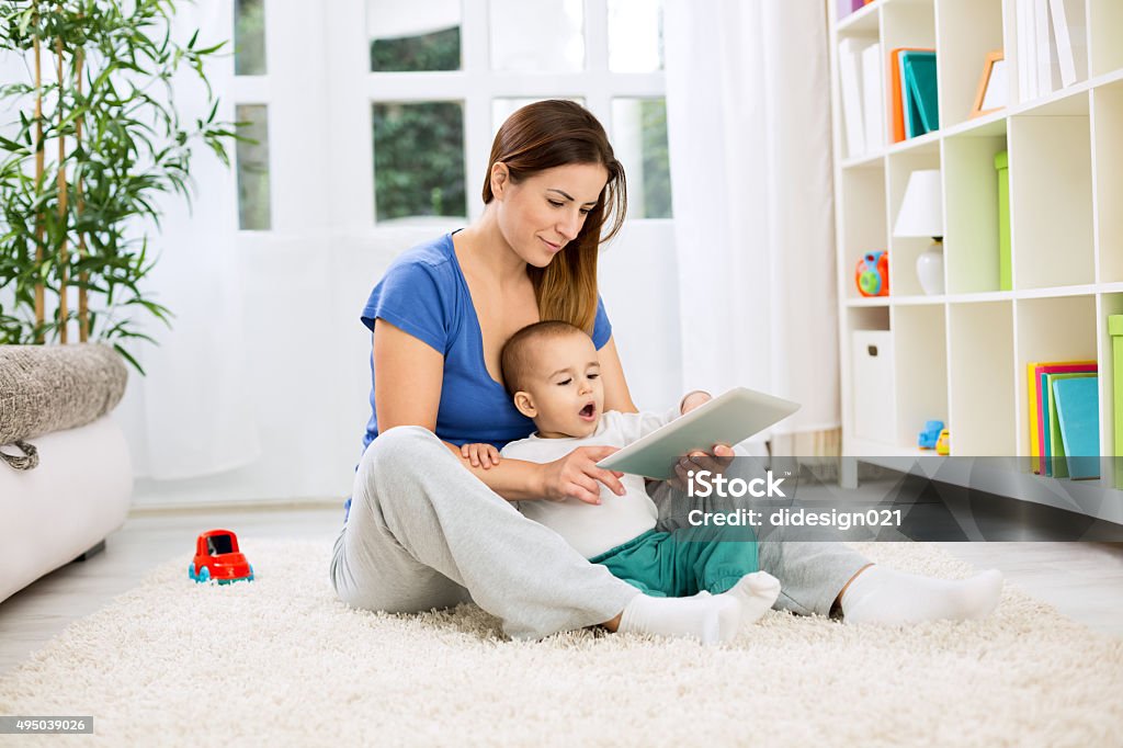 Happy smiling mother and child playing on tablet Happy smiling mother and little child playing on tablet 2015 Stock Photo