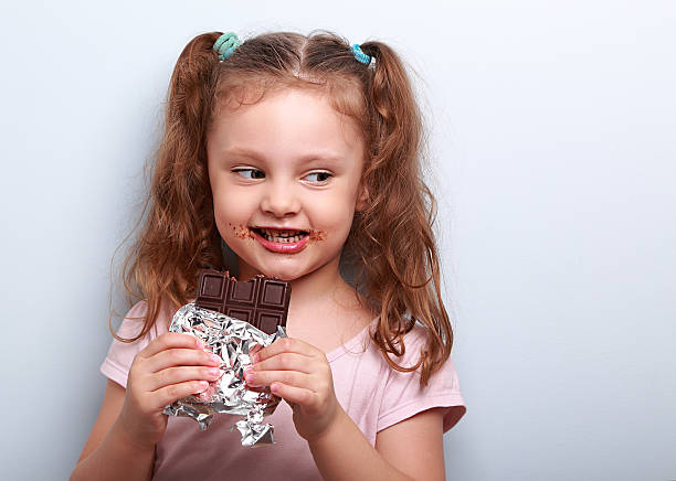 istock Curious cute kid girl eating dark chocolate and looking fun 495050264