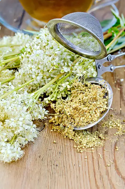 Metal sieve with dried flowers of meadowsweet, a bouquet of fresh flowers of meadowsweet, tea in a glass cup on a wooden board