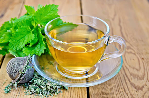 Herbal tea with melissa in a cup and strainer Herbal tea in a glass cup, metal sieve with dry mint leaves, fresh mint leaves on the background of wooden boards tea leaves stock pictures, royalty-free photos & images