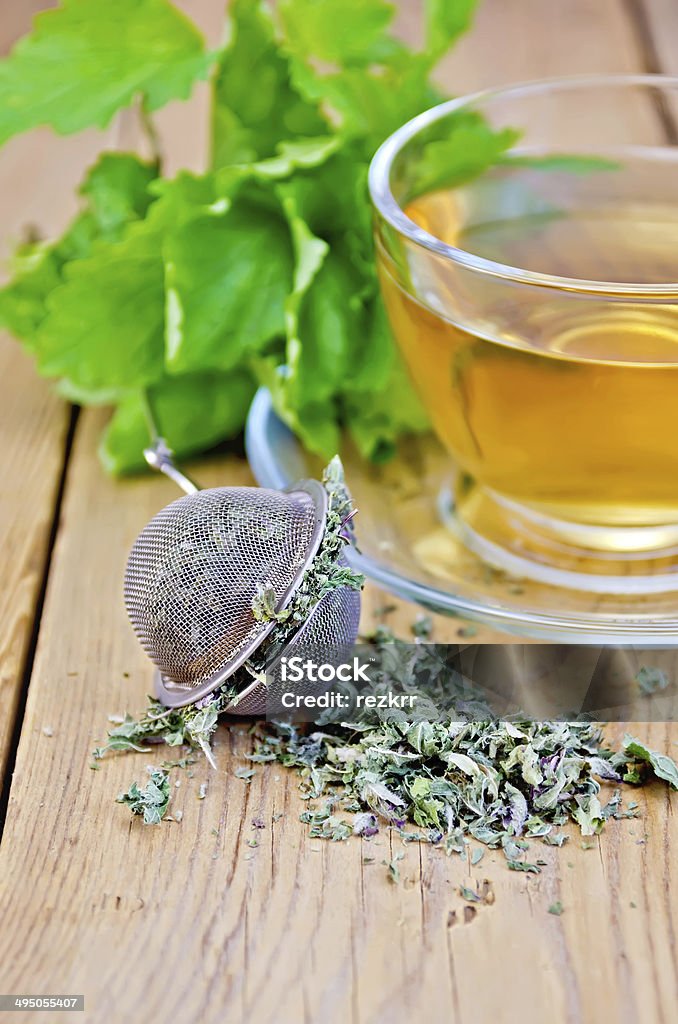 Herbal tea from melissa in cup with strainer on board Metal sieve with dry mint leaves, herbal tea in a glass cup, fresh mint leaves on the background of wooden boards Alternative Therapy Stock Photo