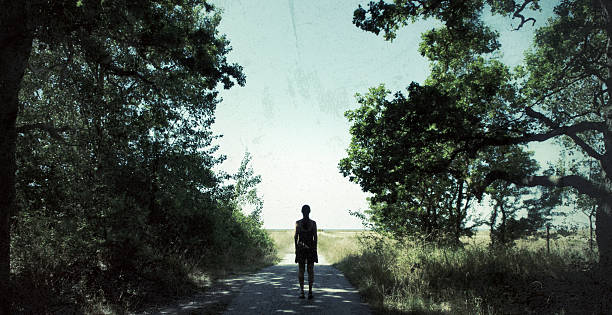 Woman standing by the edge of a forest looking towards the horizon by the sea.