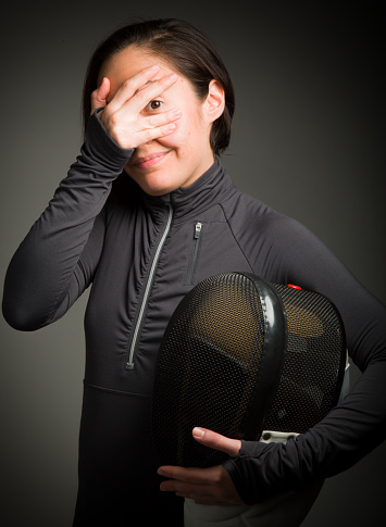 Female fencer peeking through hands covering face