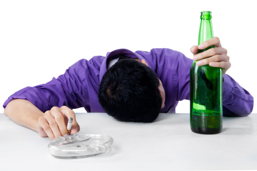 Drunk man sleeping on the table while holding cigarette, with a glass and bottle of beer