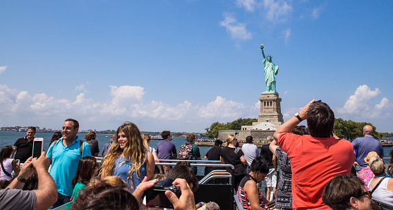 New York City, New York, USA - August 19, 2015:  View of people of Statue of Liberty sightseeing cruise boat with the Statue of Liberty in the background.  The Statue of Liberty and Ellis Island is one the most notable tourist attractions in New York City.