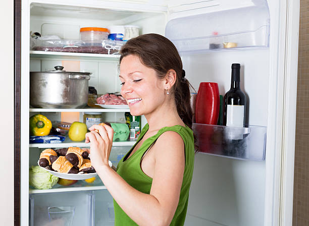 istock Woman near opening fridge eating cakes 495067706