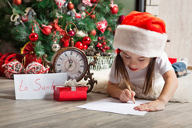 pensativo menina com chapéu de papai noel escreve carta de santa - clock baby christmas small - fotografias e filmes do acervo