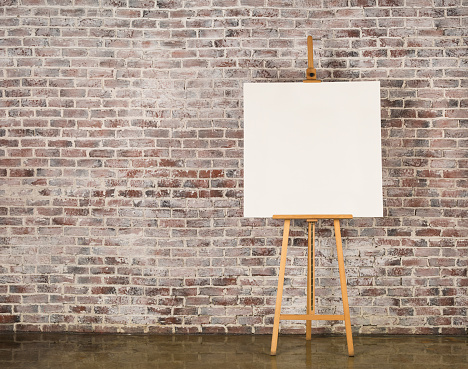 Easel with blank canvas on a brick wall background