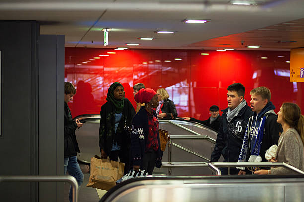 Essen, Germany - October 31, 2015: Two young black women are standing with shopping bags on upper floor of hall main station Essen. They are wearing headscarfs. Men and people are coming upstairs on steps and escalators.