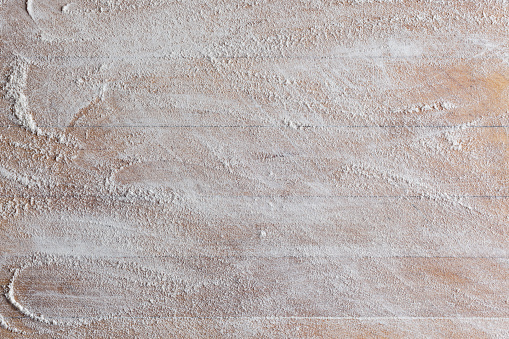 Rough wooden rectangular used cutting board background with flour directly from above closeup