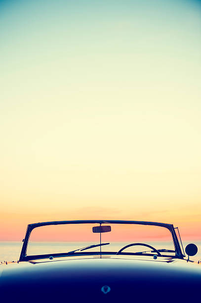 Convertible at the beach at sunset or sunrise Convertible at the beach at sunset or sunrise. Car is parked at the edge of the sand looking at the view over the ocean. No people. Copy space. Rear view. status car photos stock pictures, royalty-free photos & images