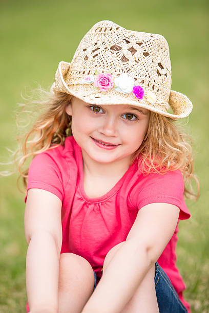 A young girl is smiling and wearing a straw hat. She is wearing a blue and pink swimsuit