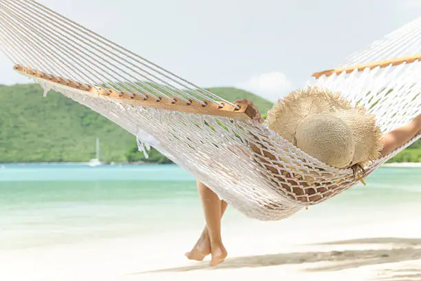 unrecognizable single young woman in summer hat relaxing in a hammock at a tropical Caribbean beach at Maho Bay, St.John, US Virgin Islands