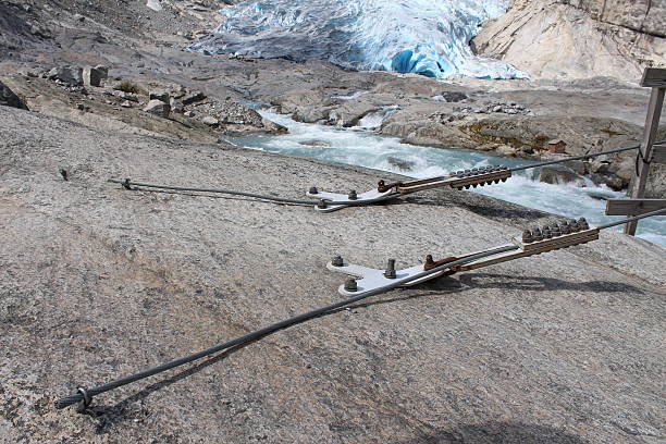 Woman sits in rocky moraine at the entrance to a intriguing turquoise ice cave and takes a picture with her smartphone while waiting to rappeli by rope into the dark blue opening under a shelf of white snowy ice with rocks during a trekking adventure on Lemon Glacier, Juneau Icefield, Juneau, Alaska, USA