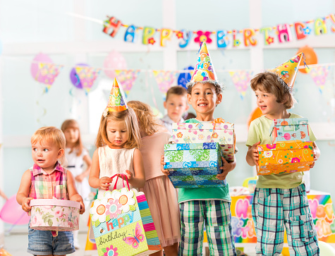 Group of happy children celebrating birthday. They are wearing birthday hats and holding gift boxes while looking at camera.