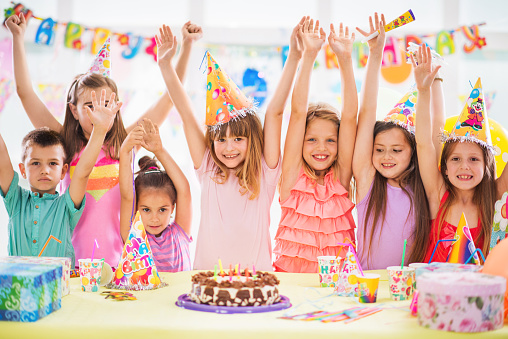 Large group of cheerful children with arms raised celebrating at birthday party.